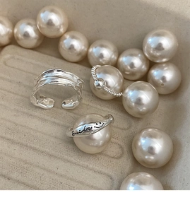 Close-up of silver wavy ring and smile engraved band set displayed with white pearls