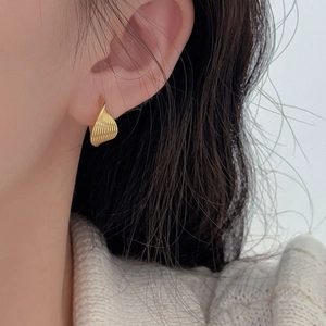 Macro detail of golden geometric twisted earrings with shell-like relief pattern