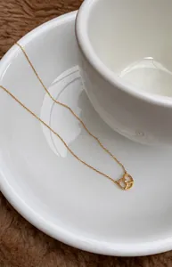 Close-up of a gold pretzel pendant necklace with white crystal on white ceramic saucer