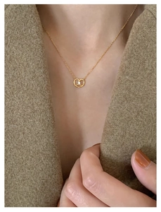 Detail of golden pretzel pendant necklace with white zircon on elegant female model