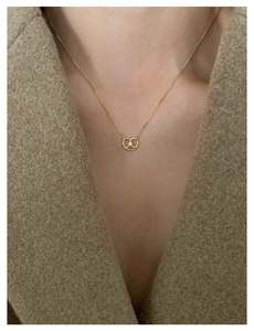 Detail of a golden pretzel necklace with a small diamond worn over a brown coat