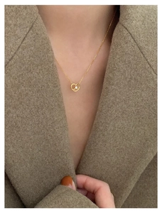 Detail of gold pretzel pendant necklace with crystal on model wearing brown wool coat