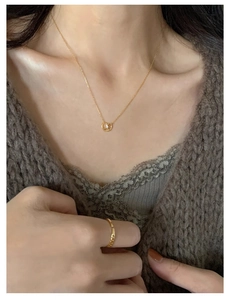 Detailed close-up of a gold pretzel pendant necklace with a white crystal stone on neck