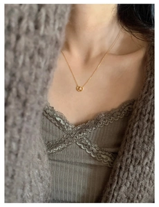 Macro shot of a golden pretzel pendant necklace with crystal detail on a model's neck