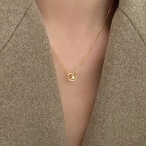 Elegant gold pretzel pendant necklace with sparkling zircon worn on camel wool fabric