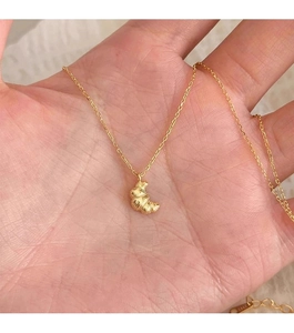 Close-up of golden croissant pendant necklace with detailed texture on fine chain