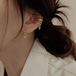 Detail of layered gold ear cuffs with zircon heart charms and quilted texture on ear