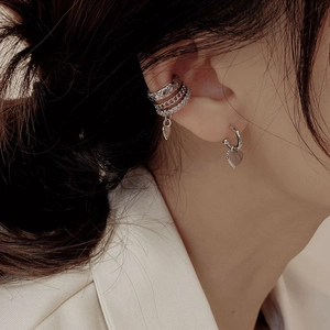 Close-up of stacked silver ear cuffs and heart pendant earring with zircon inlay