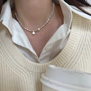 Dettaglio di ciondoli a cuore e faccina sorridente su collana di perle girocollo