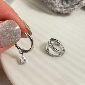 Detalle de pendientes asimétricos de plata con piedra de pera y engaste de pavé