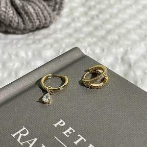 Detalle de pendientes asimétricos bañados en oro con circonitas y un colgante de pera