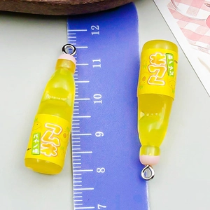 Close-up of yellow resin soda bottle charms measuring 4cm with ruler for size reference