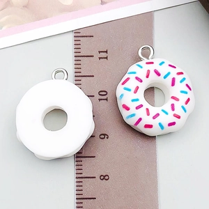 Close-up of white resin donut charms with sprinkles next to a ruler for size