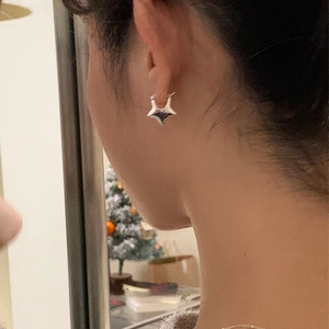 Detalle de un pendiente de aro con estrella 3D plateada usado por una modelo de lado