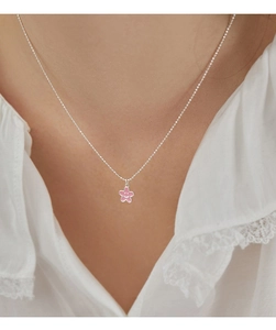 Dettaglio della collana a fiore rosa smaltato con faccina sorridente su camicetta bianca