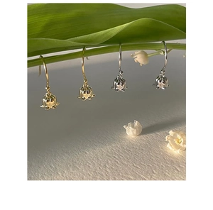 Detail view of lily of the valley earrings in gold and silver hanging on green leaves