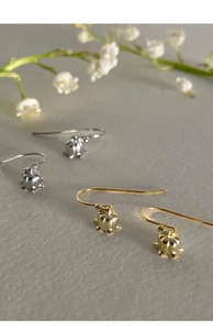 Detail shot of elegant gold and silver lily of the valley drop earrings on a textured surface
