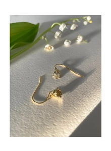 Detail of elegant lily of the valley earrings in gold finish on a textured white background