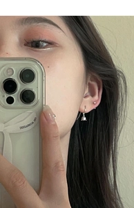 Detailed view of silver bell drop earrings and huggie hoops on ear for summer styling
