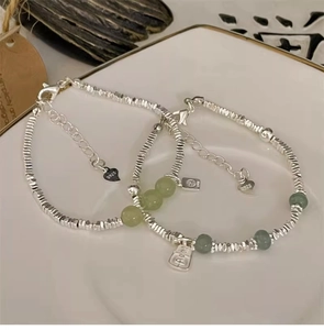 Nahaufnahme von Silberarmband mit grünen Jadeperlen und Herzanhänger in einer Schale