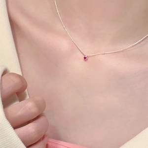 Gros plan d'un minuscule pendentif coeur rouge sur une fine chaîne argentée perlée