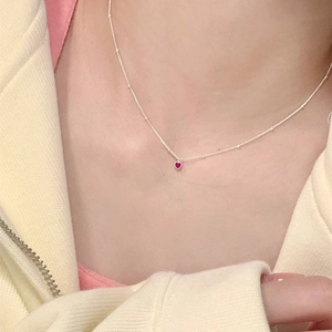 Gros plan d'un collier chaîne à billes en argent avec petit pendentif cœur rouge au cou