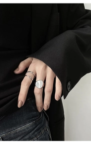 Detalle de anillos plateados de doble capa y anillo de sello ovalado con nácar en la mano
