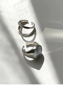 Detalle de anillo doble plateado y anillo de sello con nácar sobre seda blanca