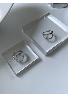 Detalle de anillos de plata trenzados con incrustación de concha en soporte acrílico