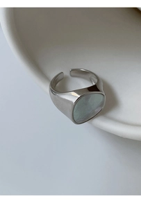 Detalle macro de anillo plateado con nácar ovalado sobre un cuenco de cerámica