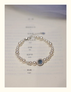 Macro detail of a pearl bracelet with a blue aquamarine pendant on an open book