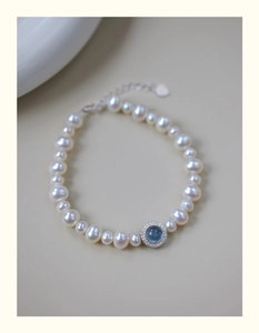 Macro detail of pearl bracelet featuring a blue gemstone pendant with a diamond halo