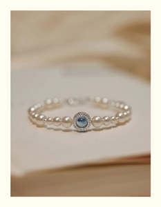 Macro detail of pearl bracelet featuring a blue gemstone pendant with zircon halo