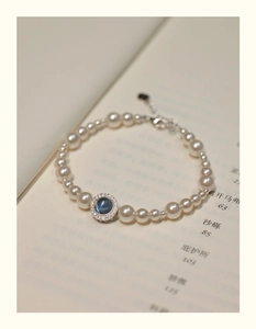 Close-up of pearl bracelet with blue stone pendant on an open book background
