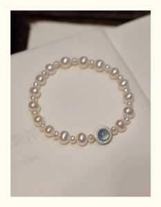 Close-up of freshwater pearl bracelet with blue zircon gemstone pendant on book pages