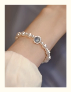 Macro detail of pearl bracelet featuring a micro-zirconia blue gemstone circular charm