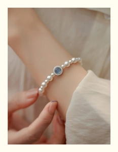 Close-up of pearl bracelet with blue gemstone pendant worn on wrist with soft lighting