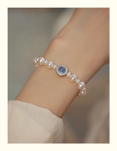 Detail of a pearl bracelet featuring a blue gemstone pendant on a model's wrist