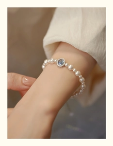 Detailed close-up of a pearl bracelet featuring a blue gemstone pendant on a model's wrist