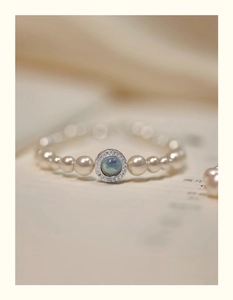 Close-up of pearl bracelet with a round blue gemstone and pavé zircon halo on a book