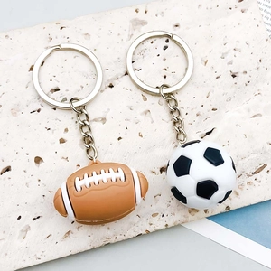 Detailed close-up of PVC football and rugby ball charms with metal keychains on stone