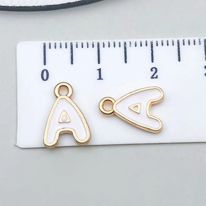 Detail of white enamel letter A charm showing 1.3cm size measurement on a scale