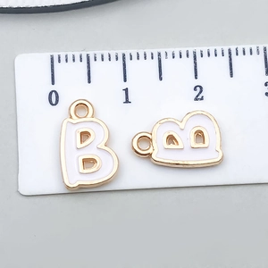 Detail view of a white enamel letter B pendant with gold edging and a ruler for size reference