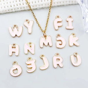 Dettaglio macro di ciondoli a lettera in smalto rosa dorato per collane e bracciali DIY