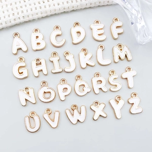 Macro detail of 26 white enamel gold-plated alloy alphabet charms for DIY jewelry making