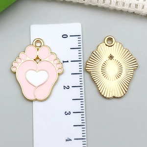 Detalle de dijes de huella de bebé rosa con esmalte y reverso de metal dorado tallado