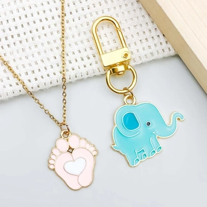 Detalle de colgantes de bebé con cadena dorada, dije de pie rosa y elefante azul