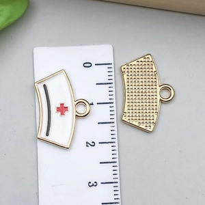 Détail du pendentif chapeau d'infirmière en émail blanc avec croix rouge et dos doré
