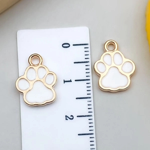 Detailed size view of two white enamel cat paw charms with gold metal frames and rulers