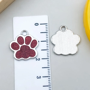 Macro detail of red glitter cat paw pendant showing polished metal texture and size scale